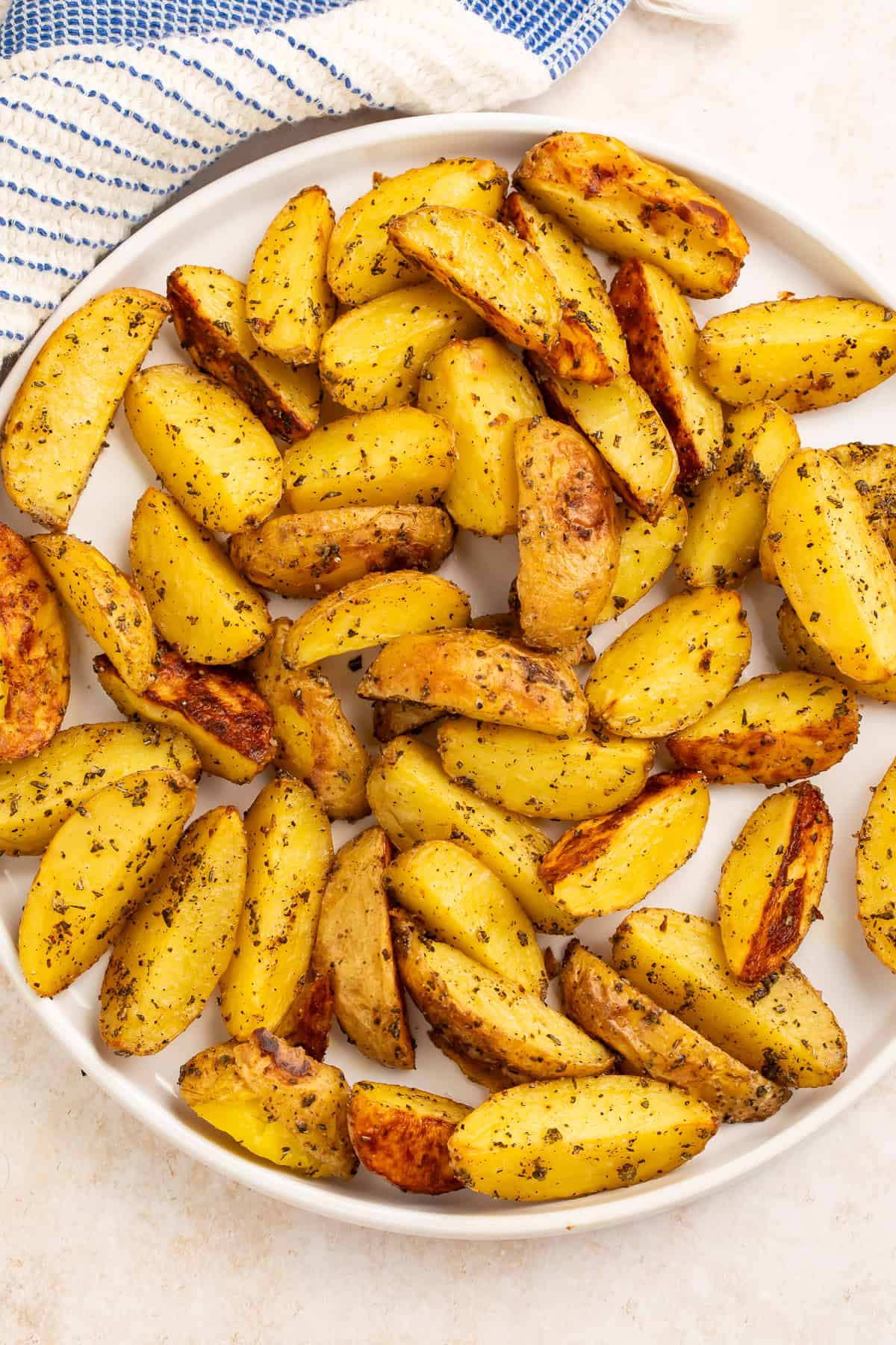White serving dish of rosemary potato wedges with a blue and white kitchen towel off to one side.