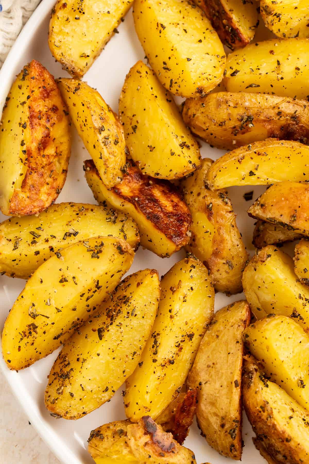 Close up of potatoes roasted with herbs in a white serving dish.