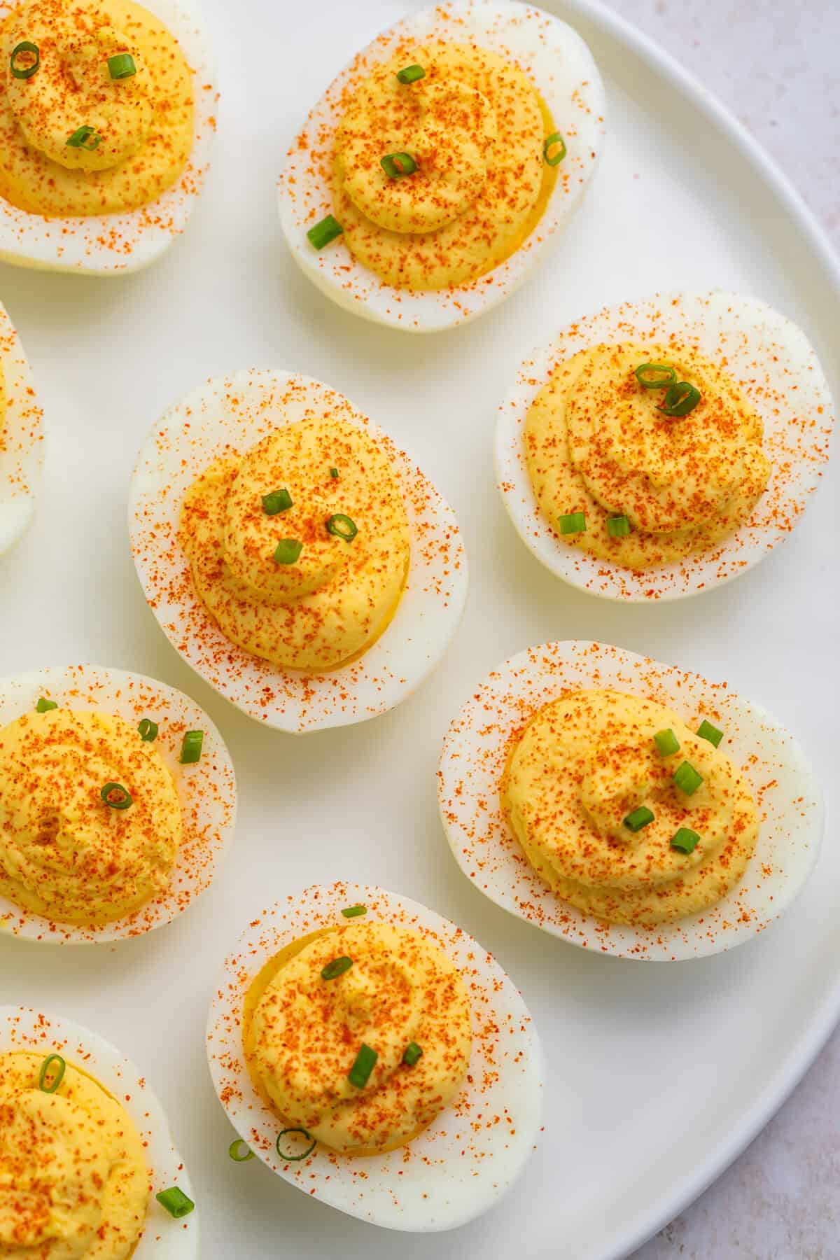 White plate of deviled eggs topped with paprika and green onion pictured top down.