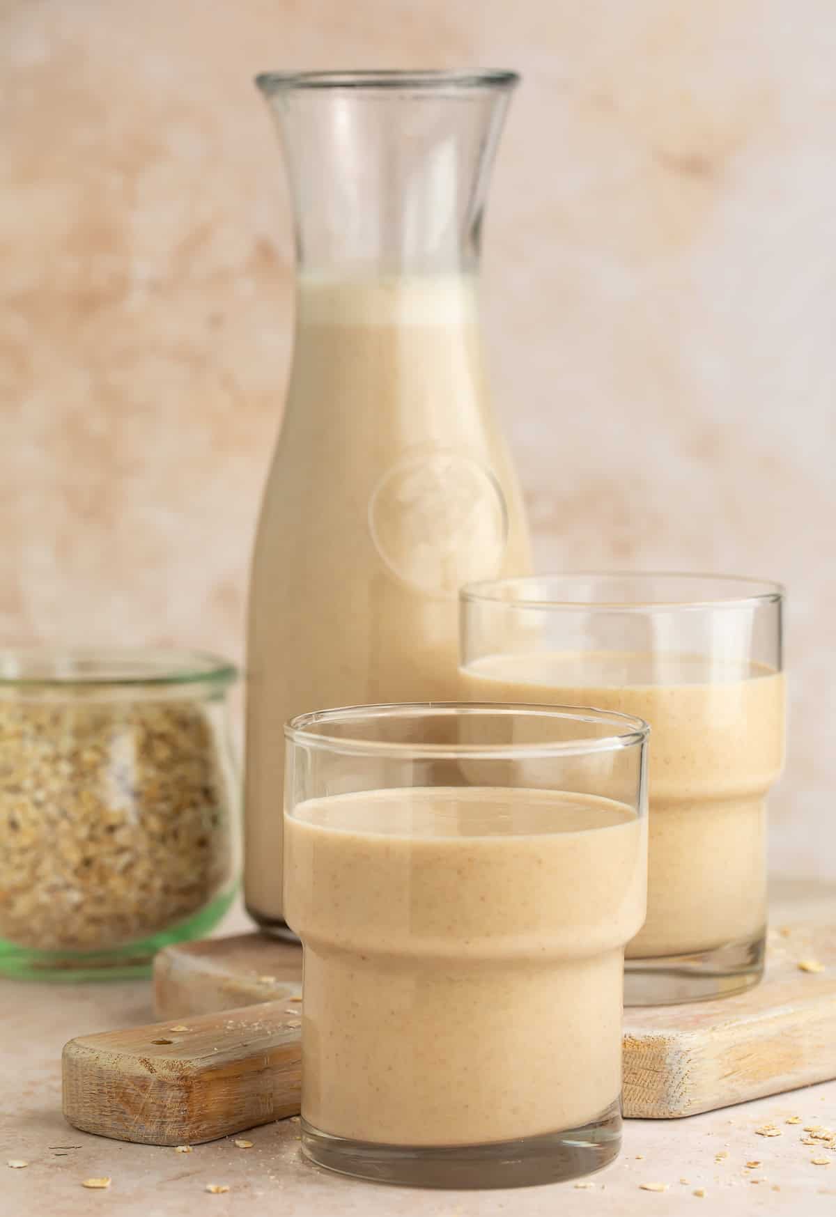 Two glasses of oat milk in front of a pitcher of it.