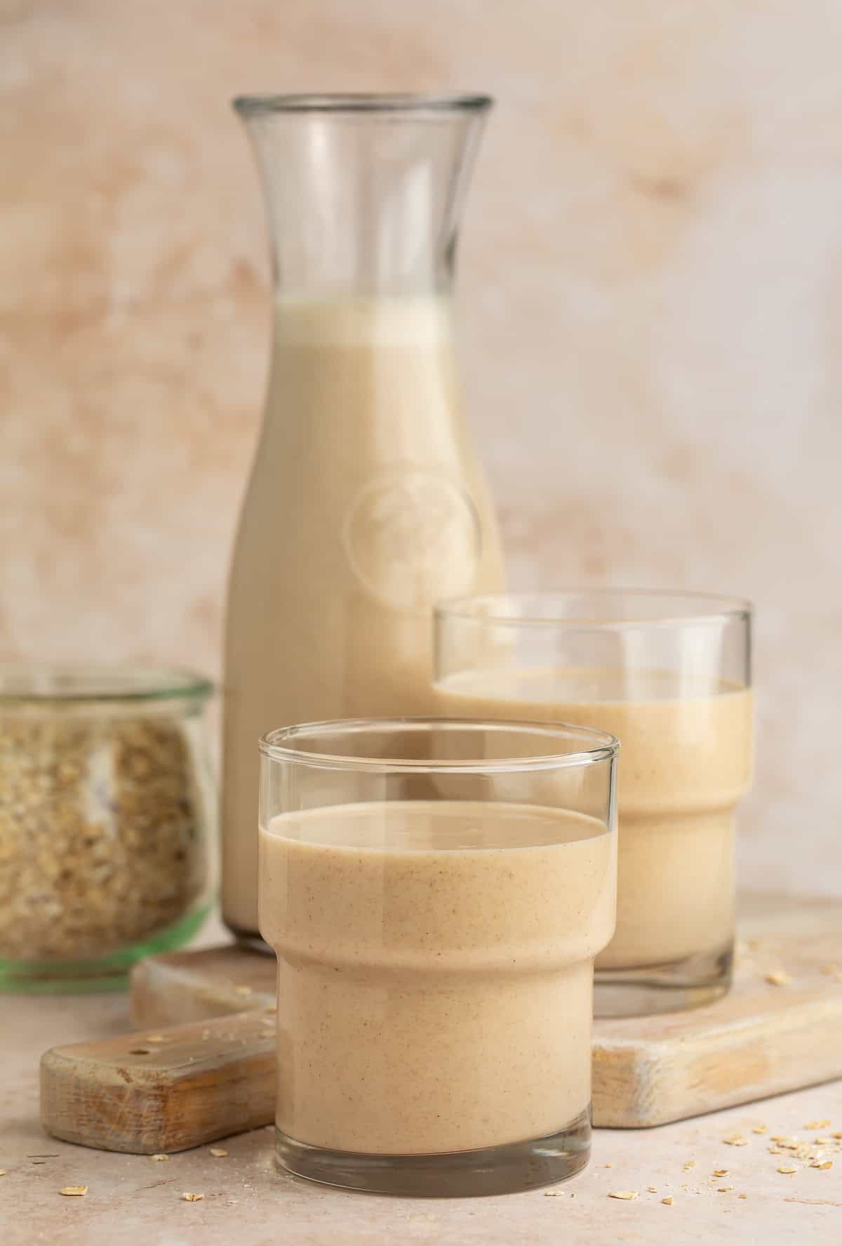 Glass of oat milk with a glass pitcher and another glass of oat milk in the background.