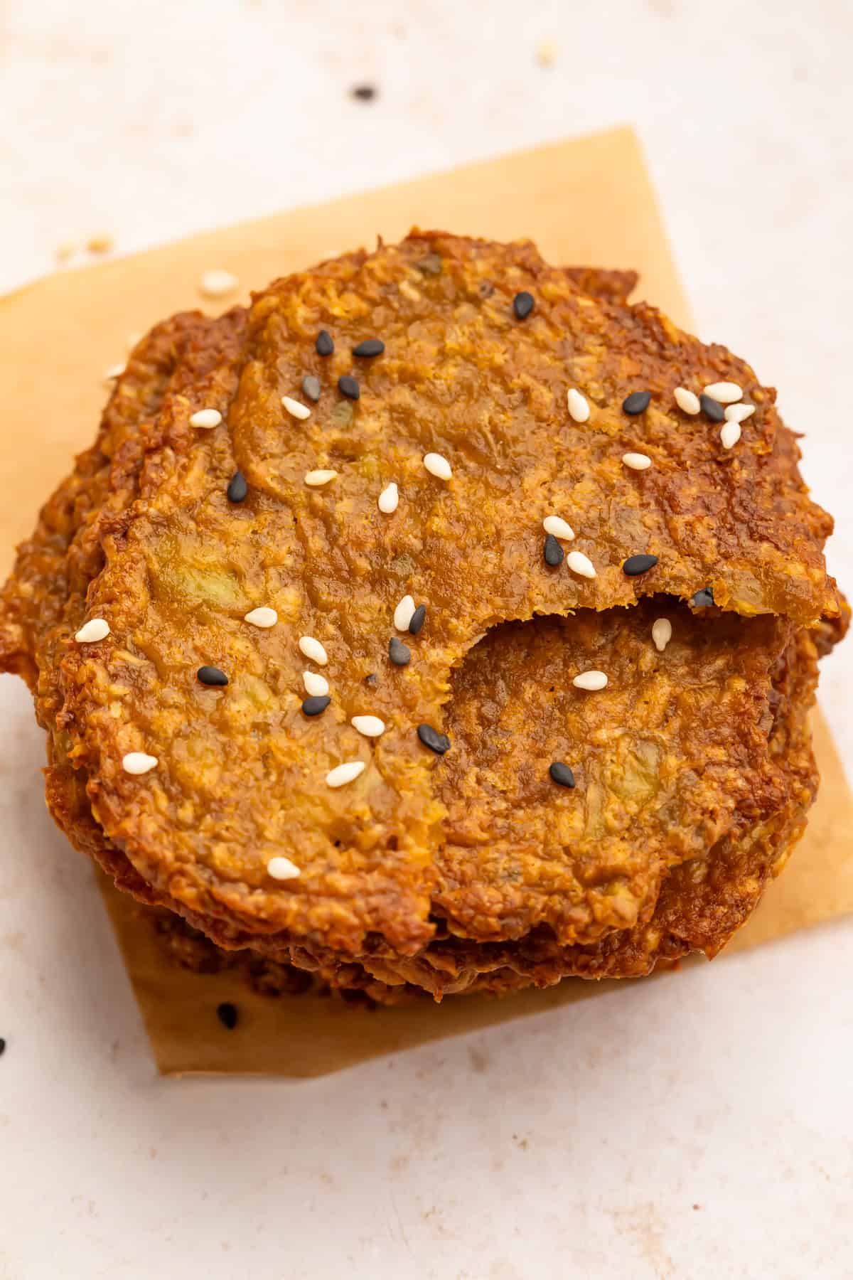 Top down view of a stack of avocado chips topped with mixed sesame seeds. The top chip has had a bite taken out of it.