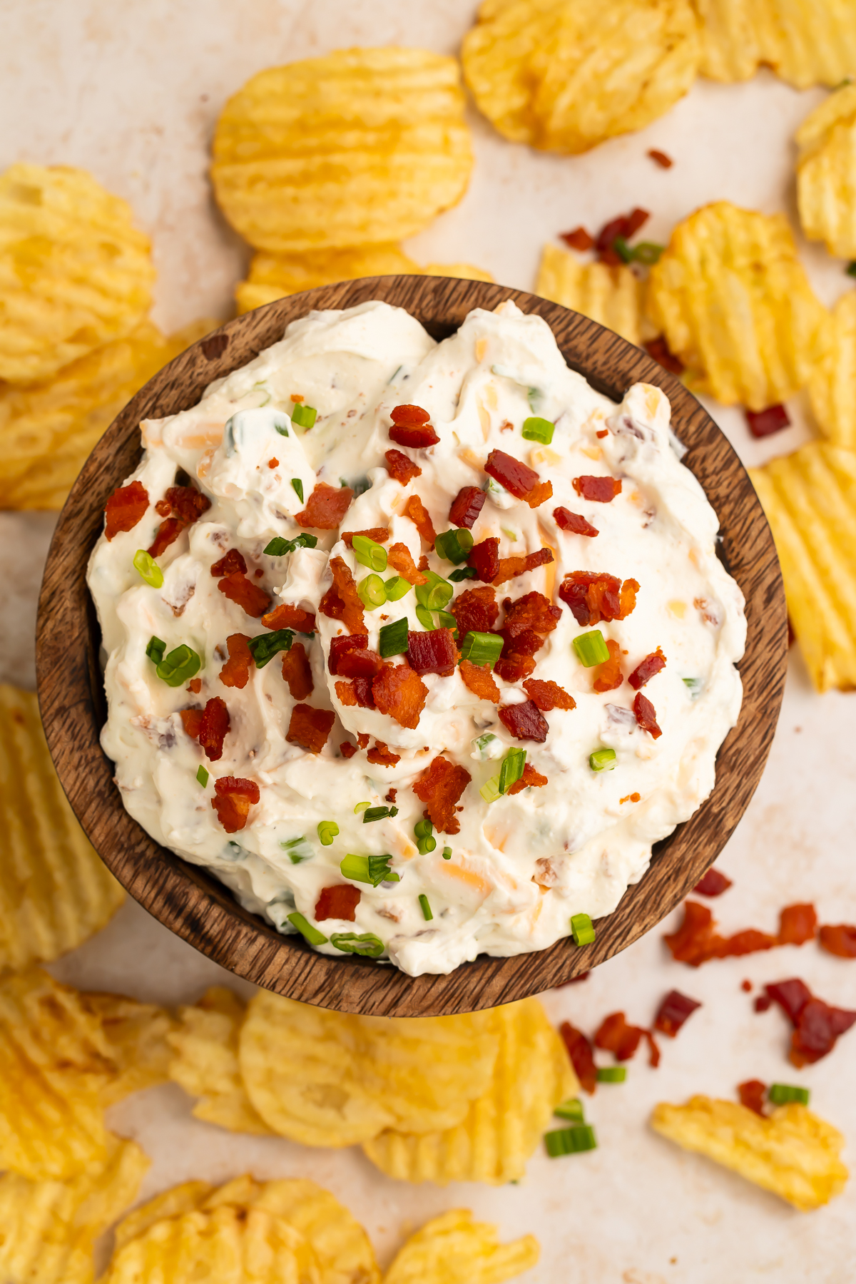 Overhead image of a baked potato dip loafed with bacon bits and green onion, with potato chips scattered around the bowl.