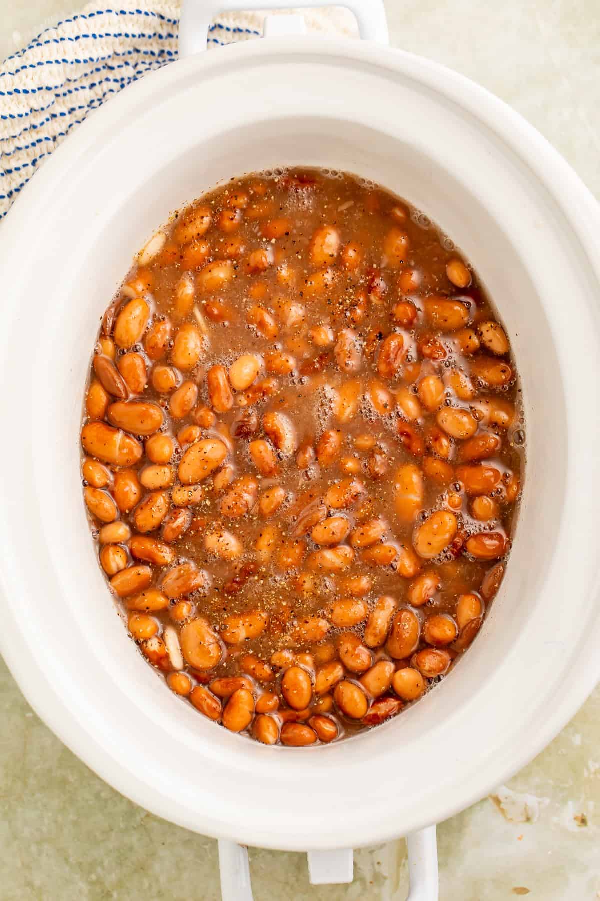 Overhead shot of cooked pinto beans in a white slow cooker insert.