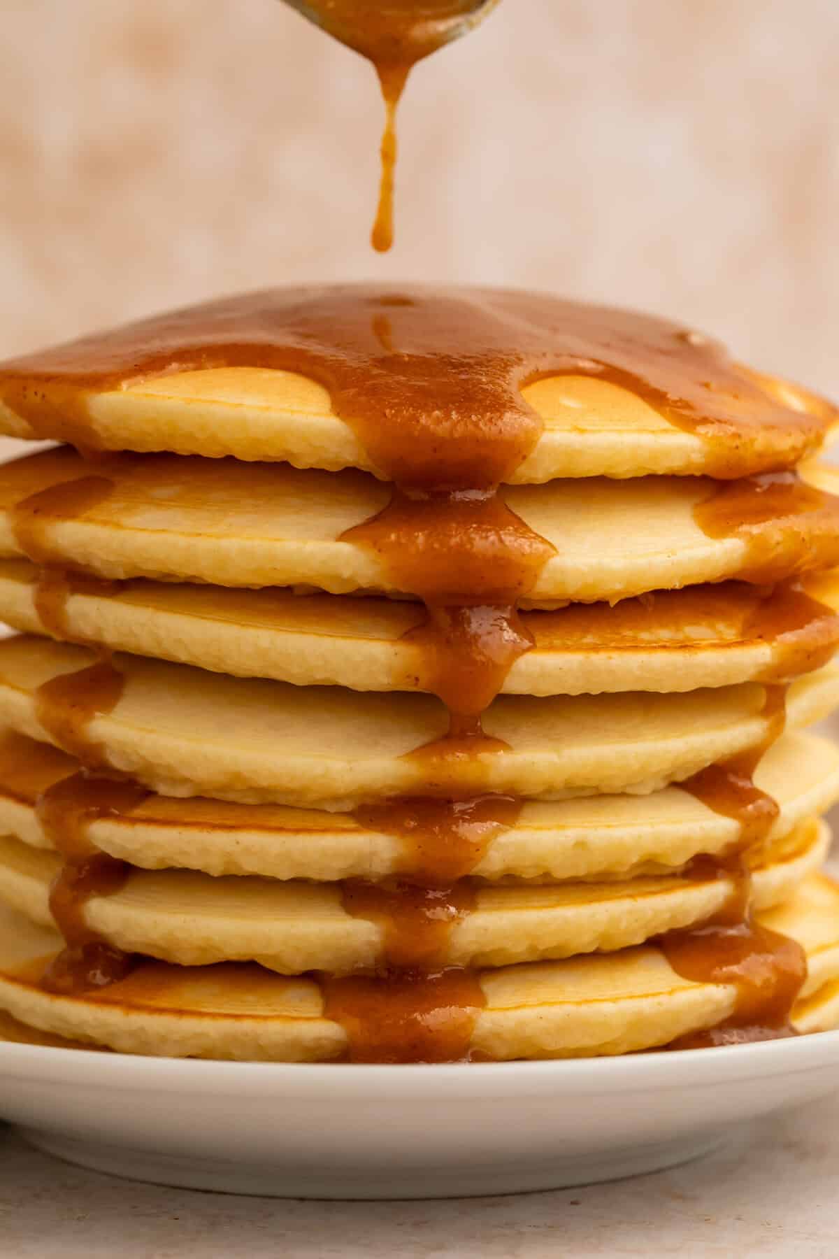 The very tip of a spoon is just visible dripping peanut butter syrup onto a stack of pancakes.