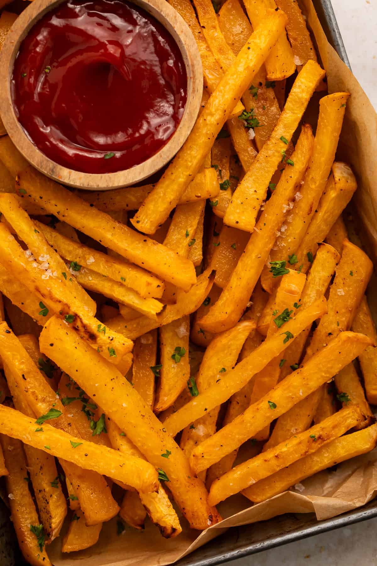 Tray of rutabaga fries with a wooden ketchup bowl nestled amongst them.