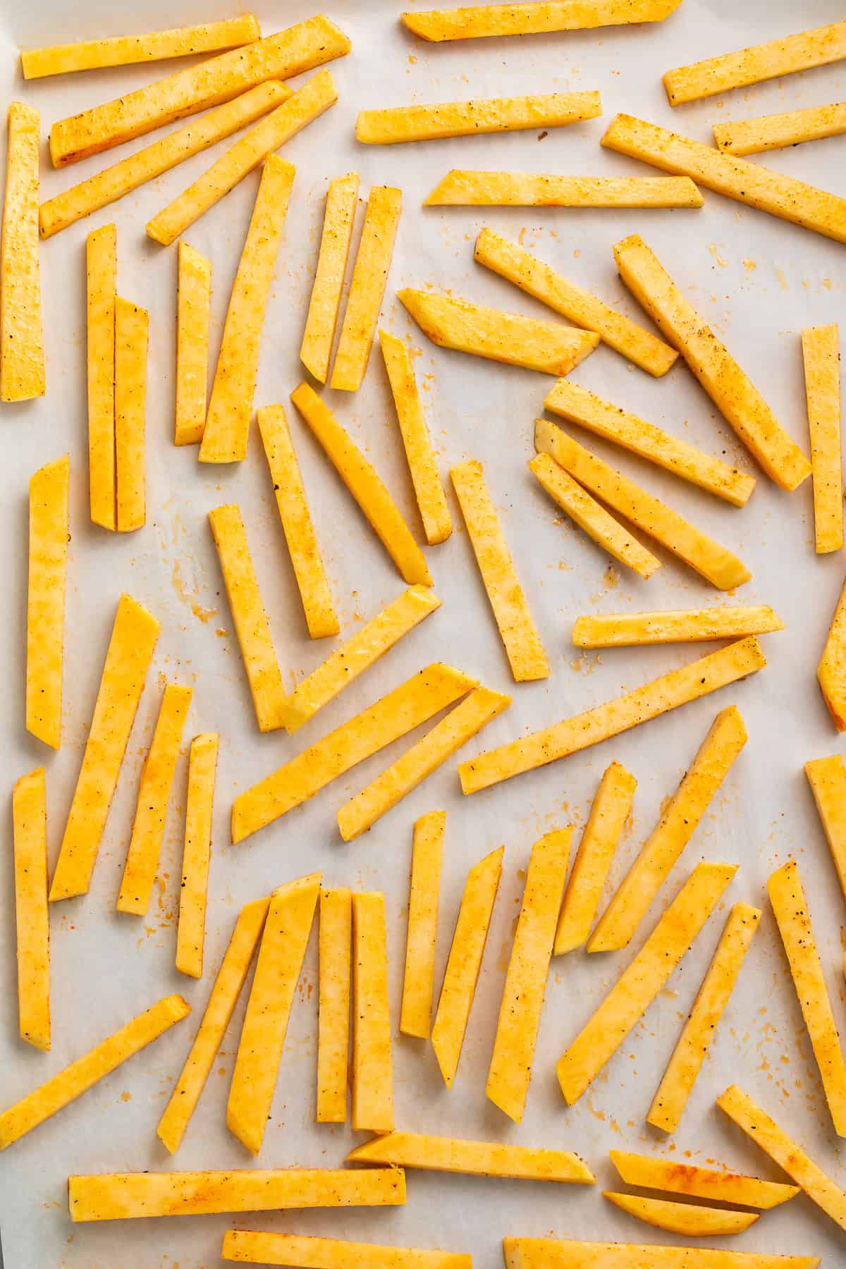 Uncooked rutabaga fries spread on a baking sheet.