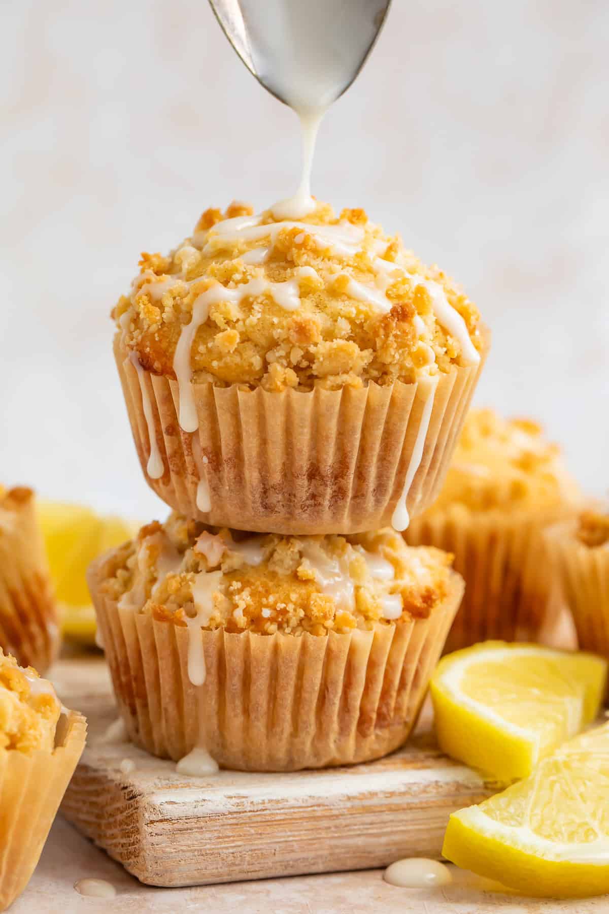 Lemon muffins stacked on top of each other with a spoon drizzling glaze on top.