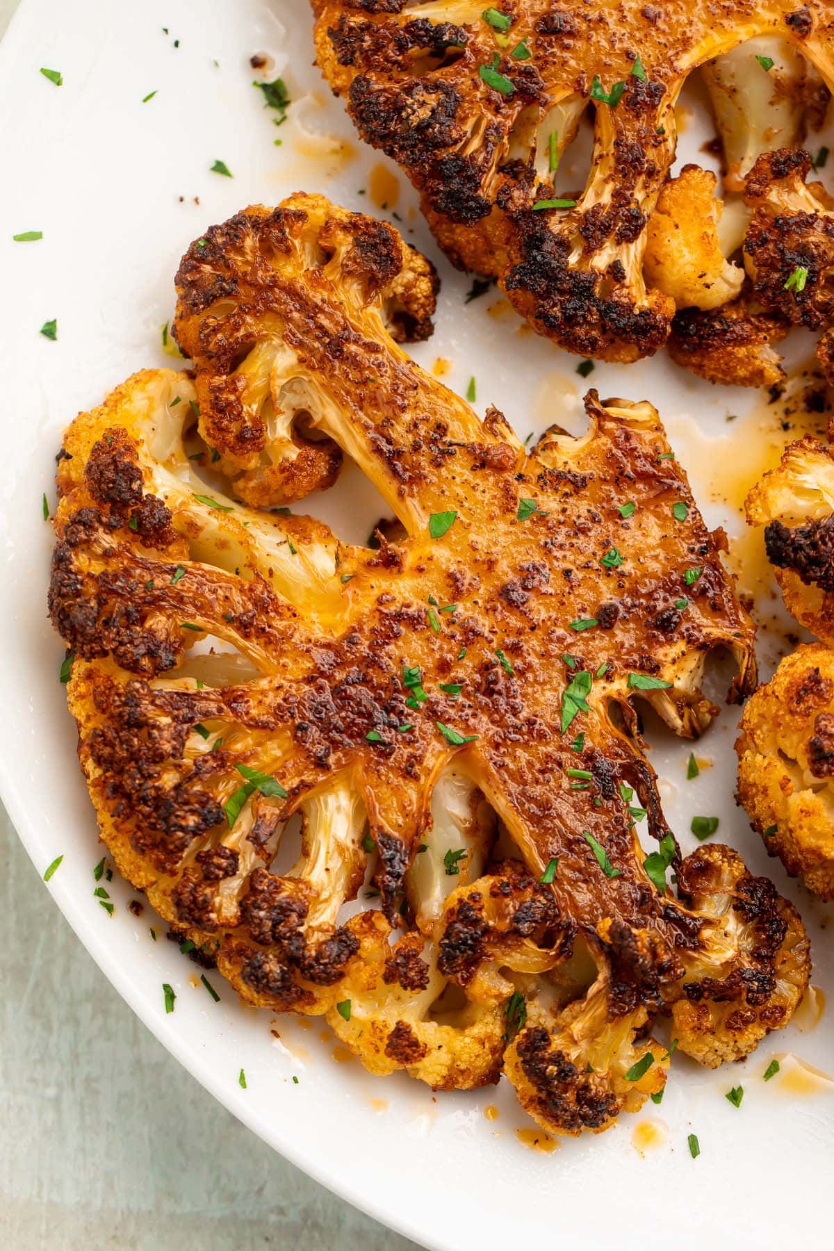 Close up of a charred cauliflower steak on a white plate.