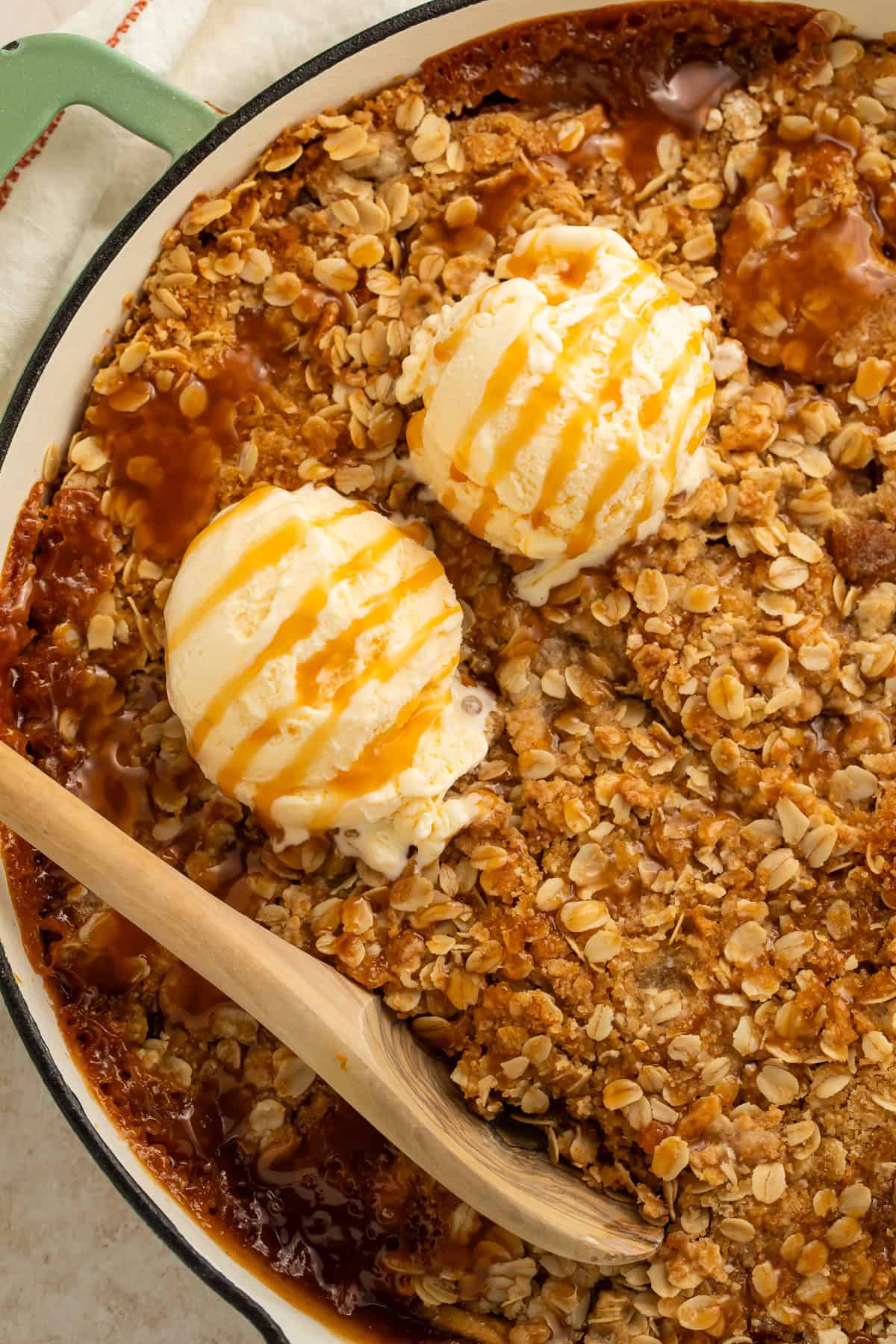 Vegan apple crisp in a green shallow skillet topped with two scoops of vanilla ice cream and caramel sauce.