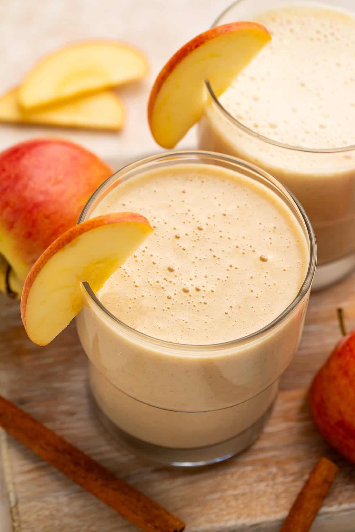 Close up of a pair of apple smoothies; the glasses are garnished with thin apple slices.