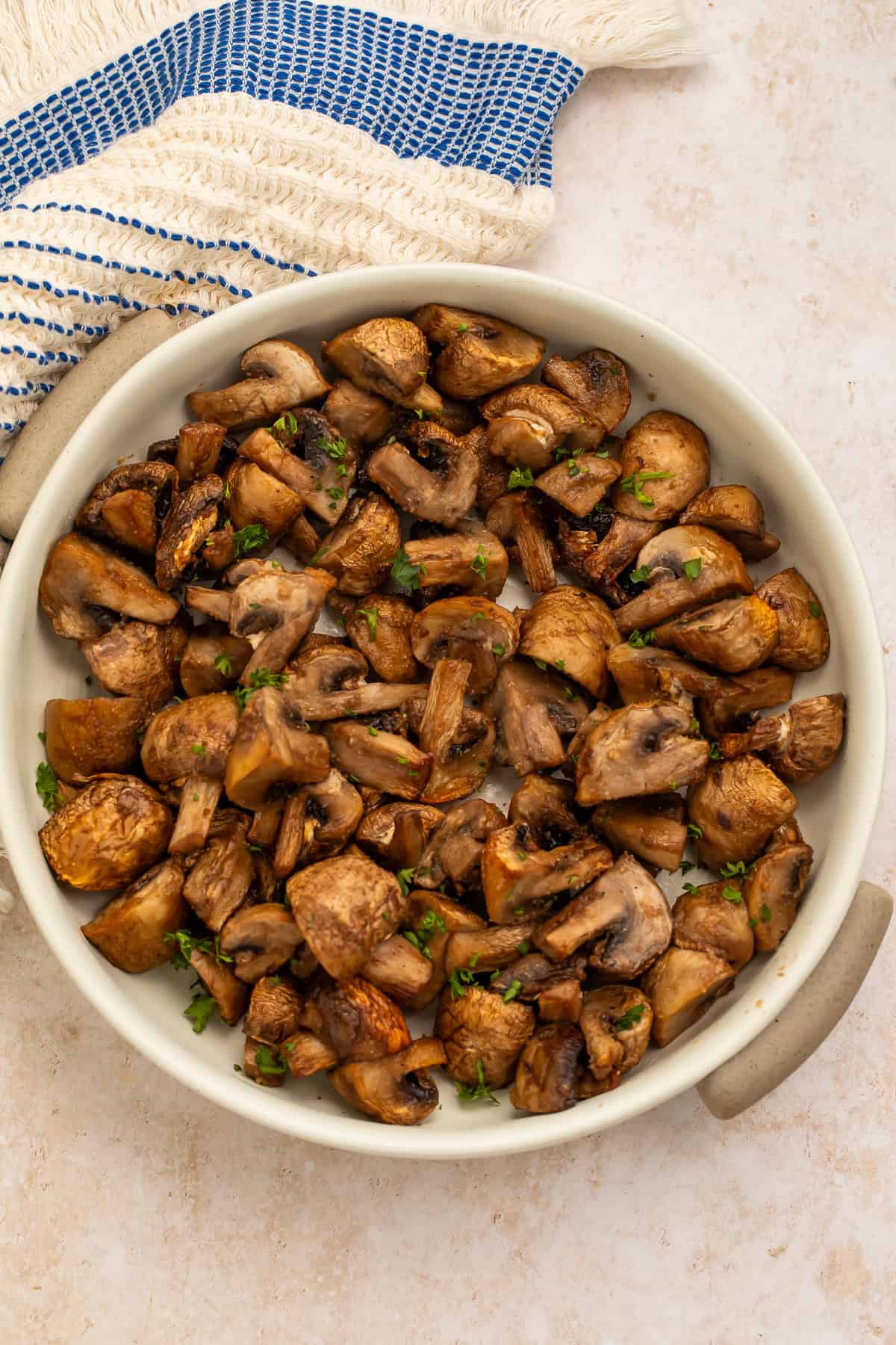 White bowl of air fryer mushrooms with a blue and white kitchen towel off to one side.