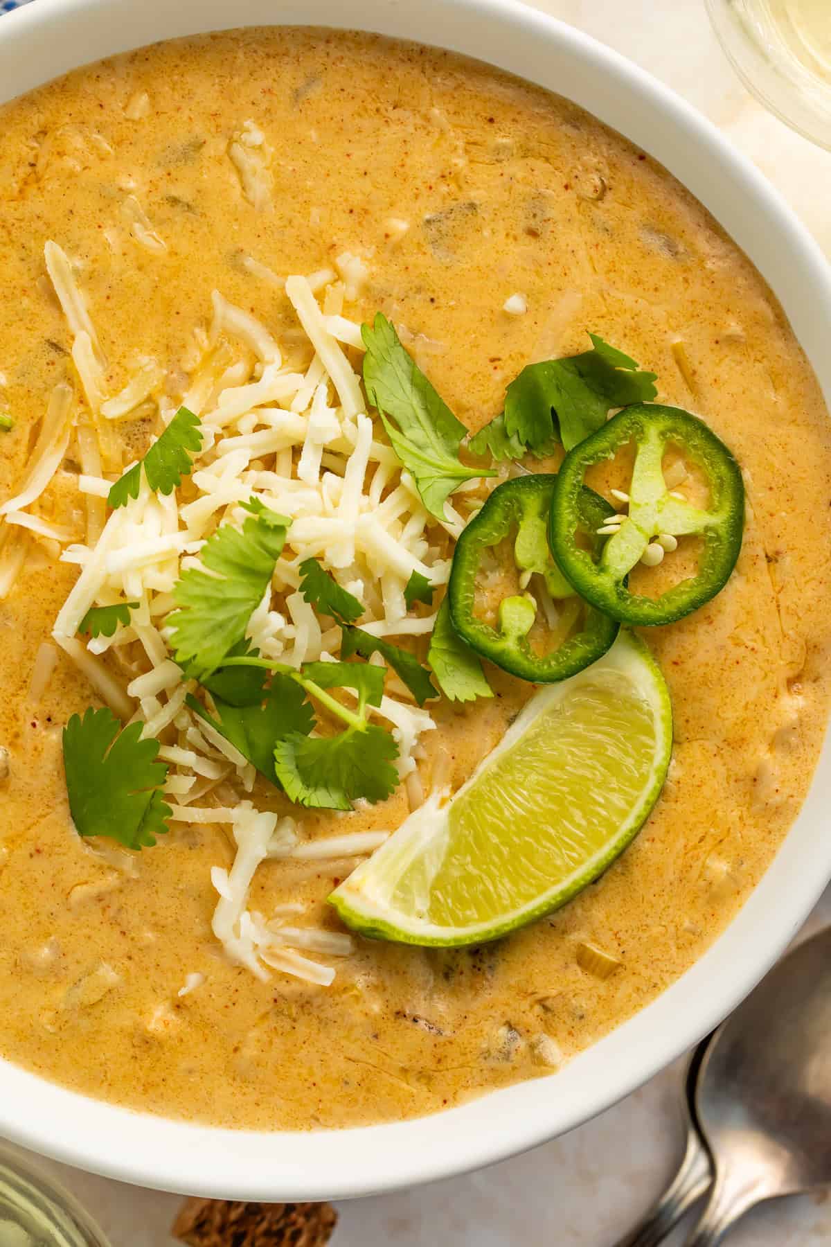 Close up bowl of keto white chicken chili topped with shredded cheese, cilantro and lime.