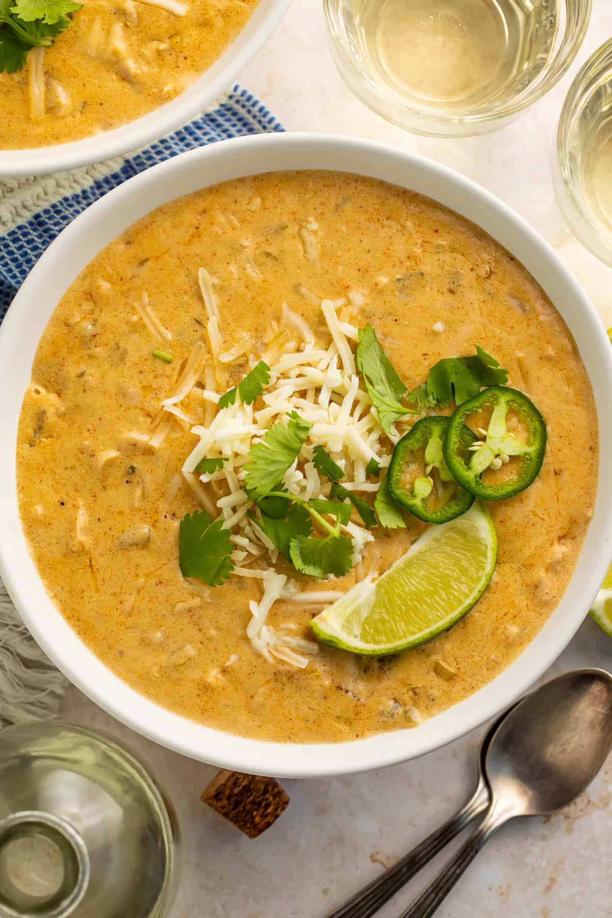 Bowl of shredded white chicken chili topped with lime, cilantro, shredded cheese and sliced jalapeno.