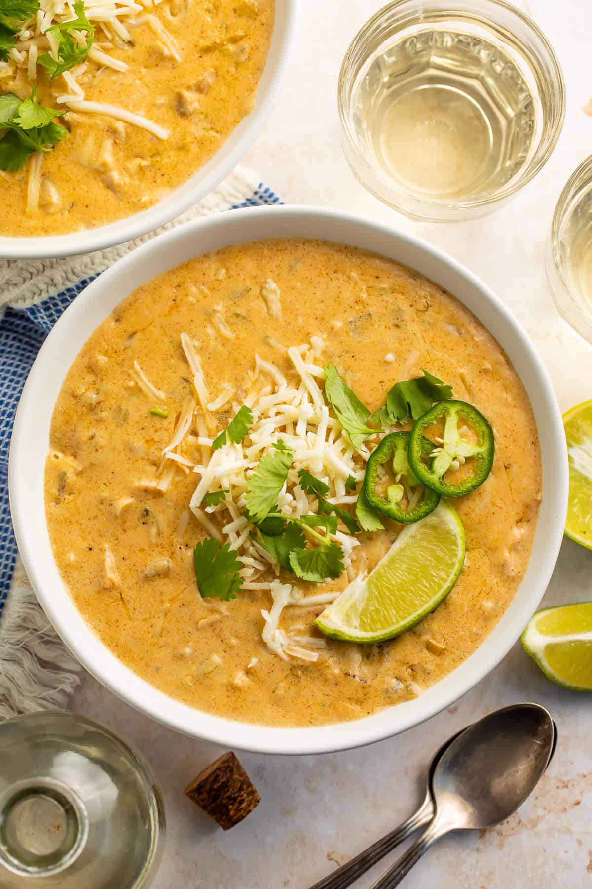 Bowl of white chicken chilli topped with shredded cheese, sliced jalapeno, cilantro and a lime wedge.