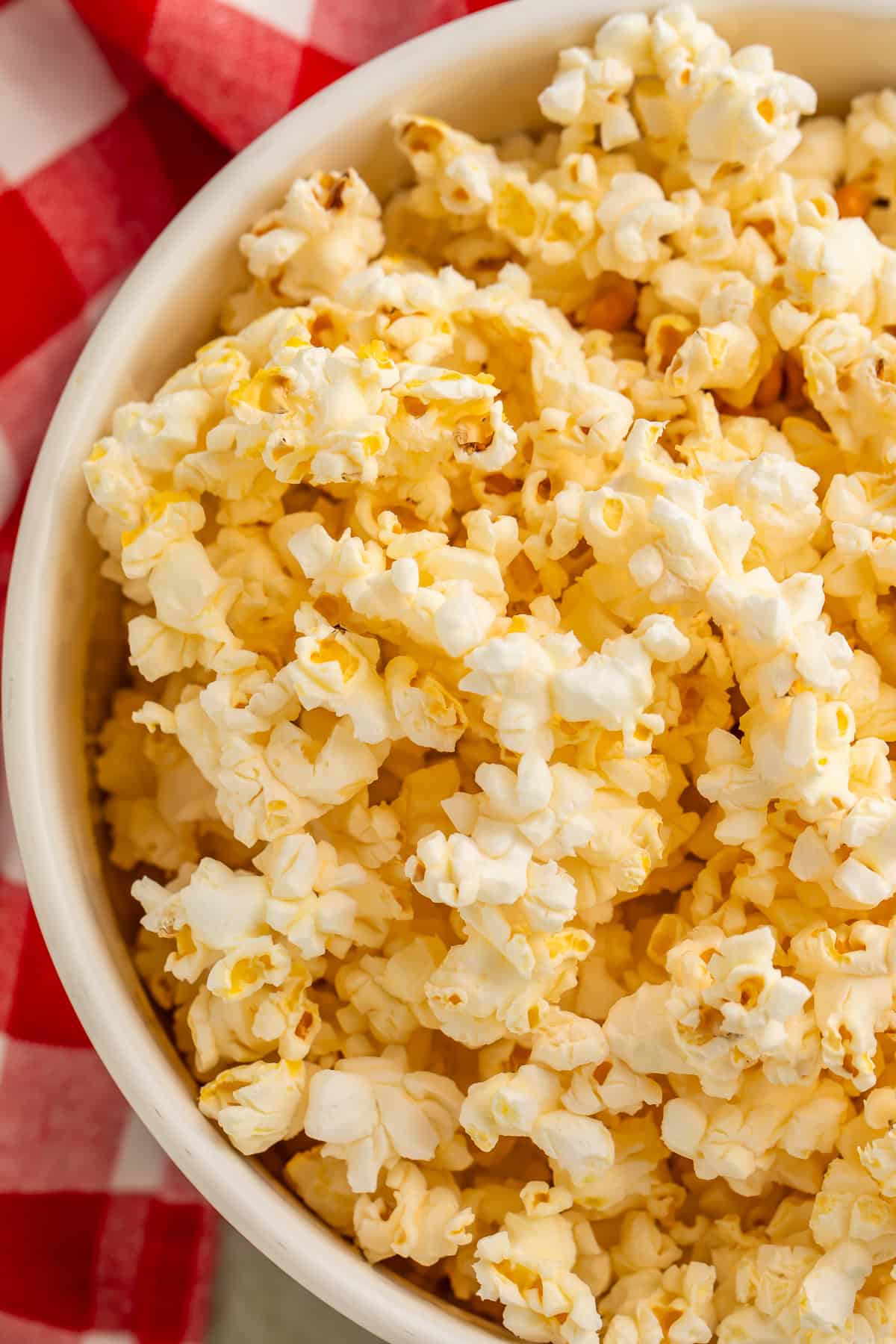 Overhead image of air fryer popcorn in a white serving bowl resting on a red and white checked cloth.