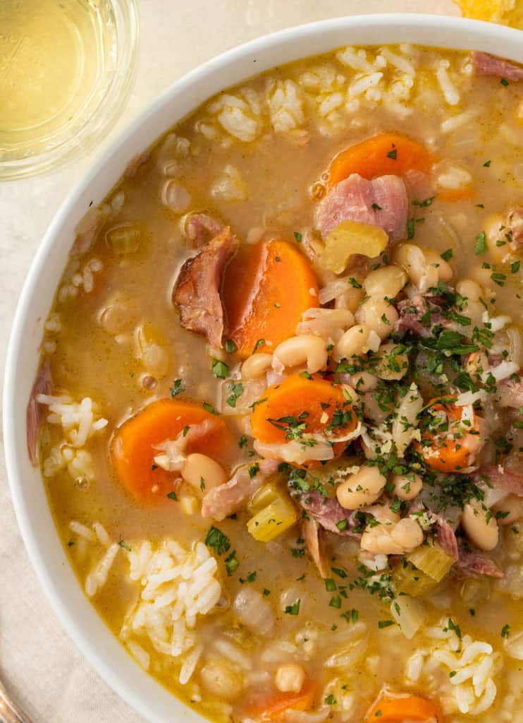 Close up of a bowl of smoked turkey and white bean soup with slices of carrot and celery, and white rice in the broth.