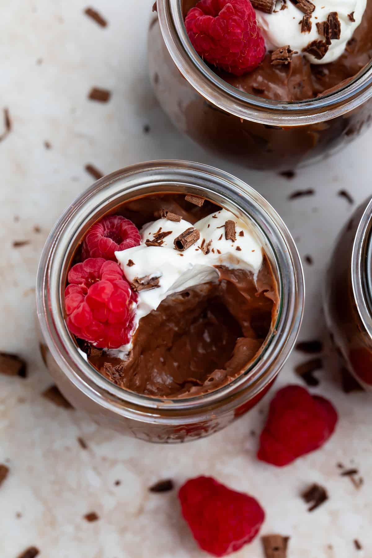 Overhead picture of two keto chocolate puddings topped with whipped cream, fresh raspberries and chocolate shavings.
