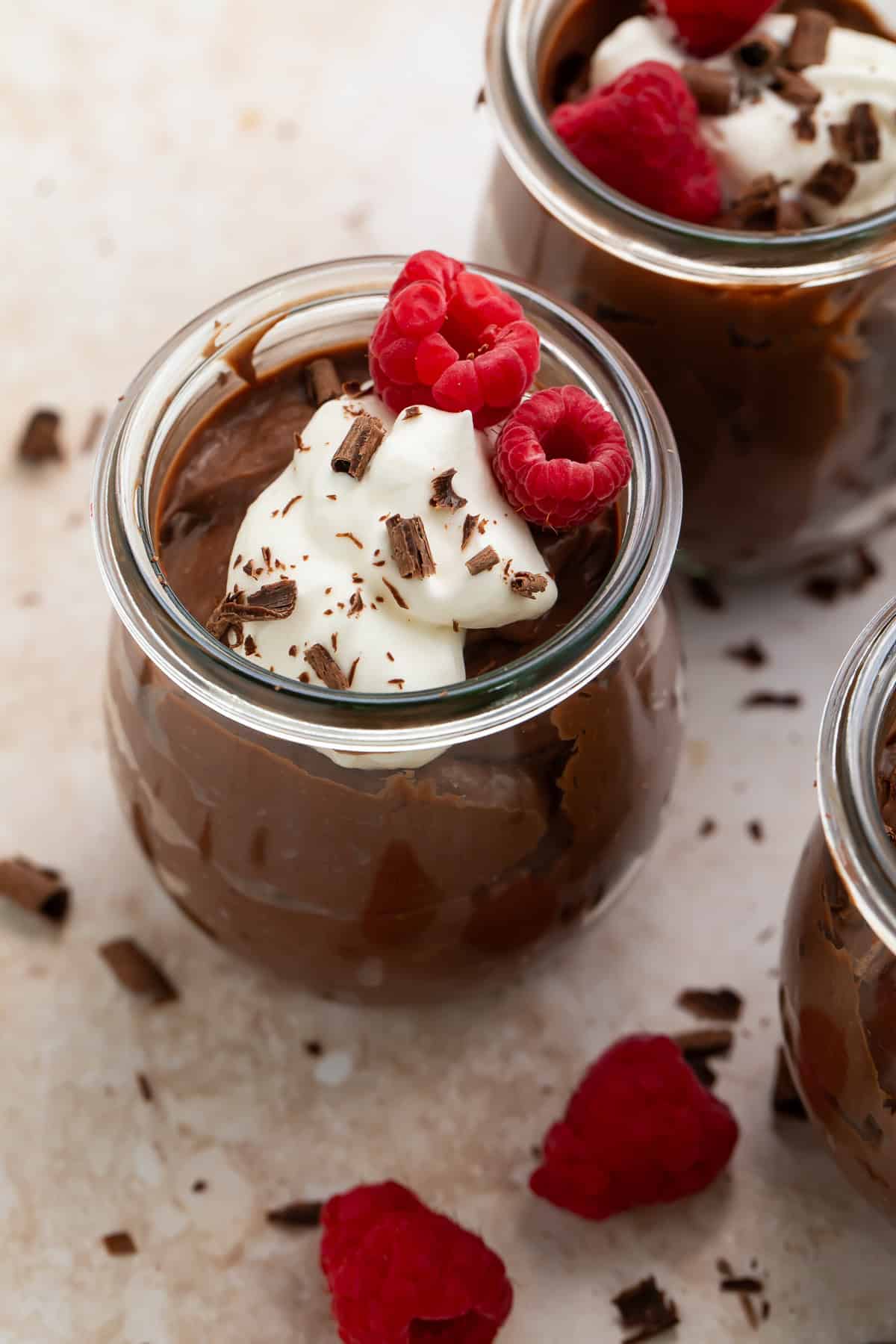 Close up of a pot of keto chocolate pudding topped with fresh raspberries, whipped cream and chocolate shavings.