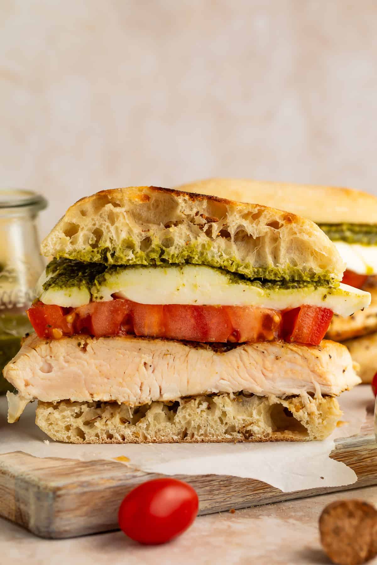 Side on close up of a sliced chicken sandwich with pesto, mozzarella and tomato.