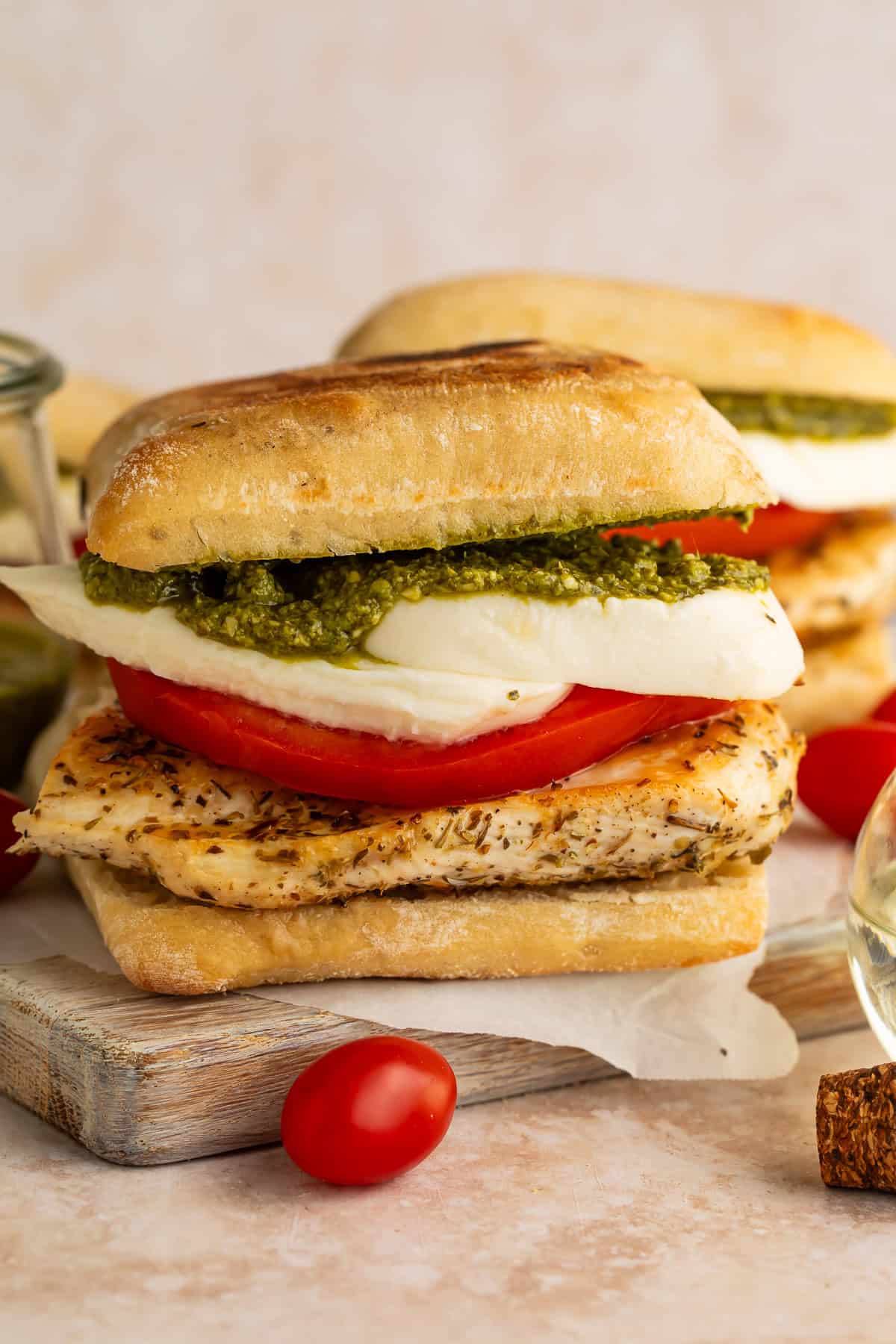 Two chicken, pesto, mozzarella and tomato ciabatta sandwiches on a wooden board.
