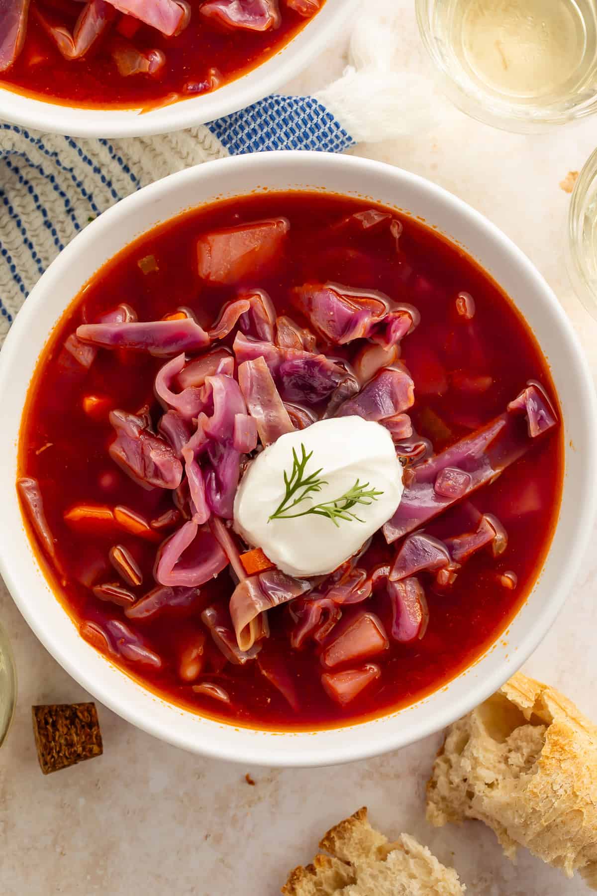 Bowl of red cabbage and bean soup with a dollop of sour cream and a sprig of dill on top.