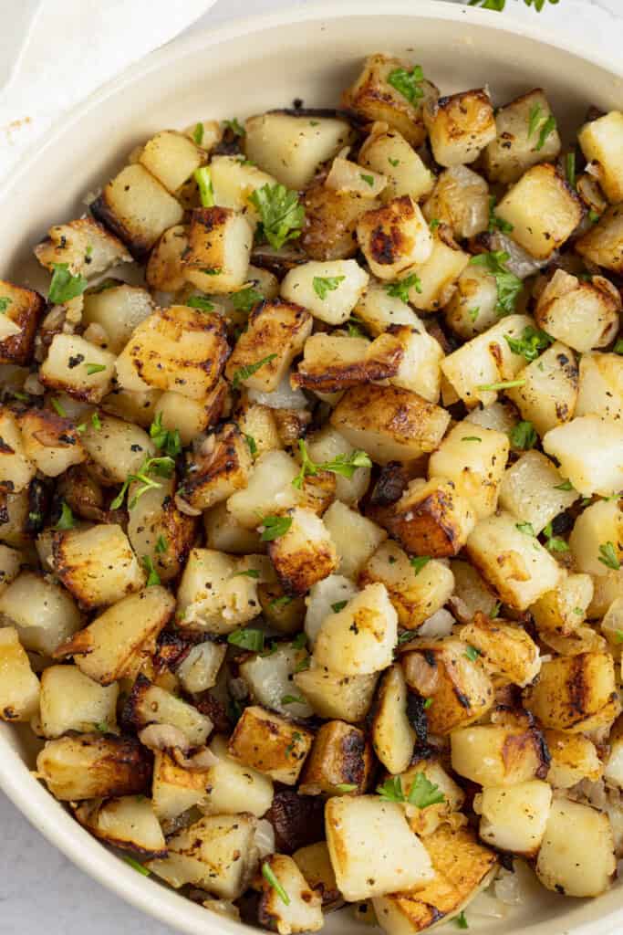 Close up of a white bowl of Southern fried potatoes with a sprinkling of chopped flat leaf parsley.