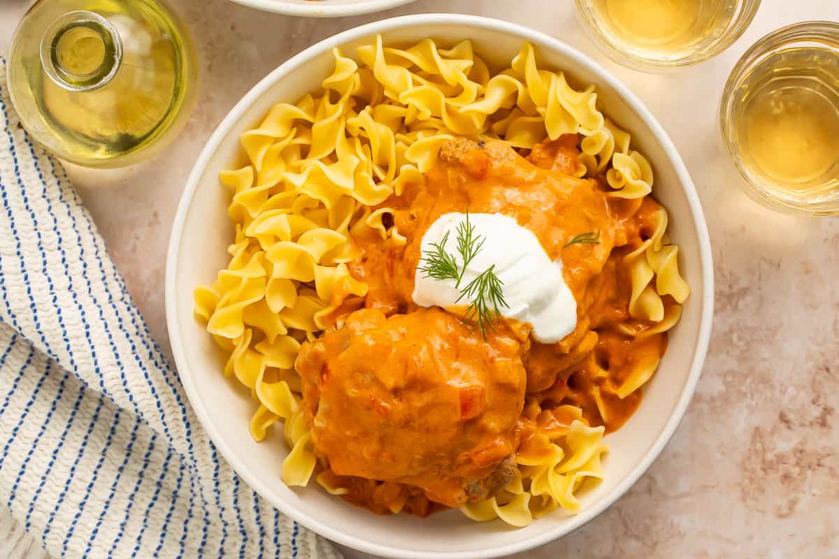 Close up of a bowl of chicken paprikas served over egg noodles, topped with dill and sour cream.