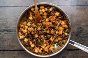 Large skillet with empanada filling ingredients on a wooden background.