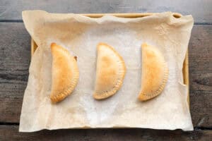 Overhead view of baked empanadas on a baking sheet lined with parchment paper.