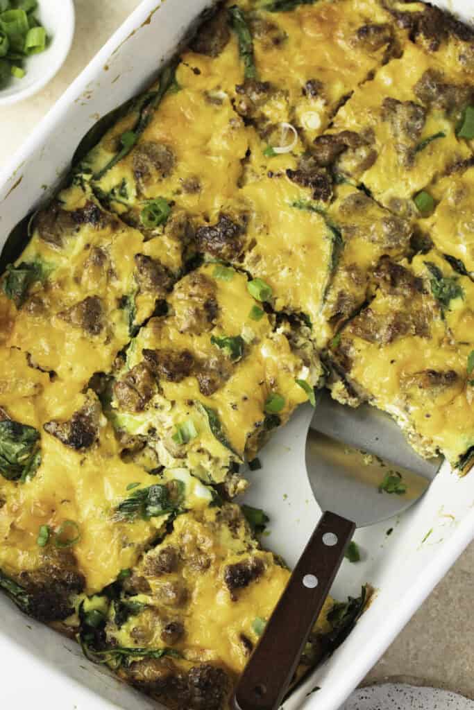 Close up of a sausage and egg breakfast casserole with a slice missing and another being removed.