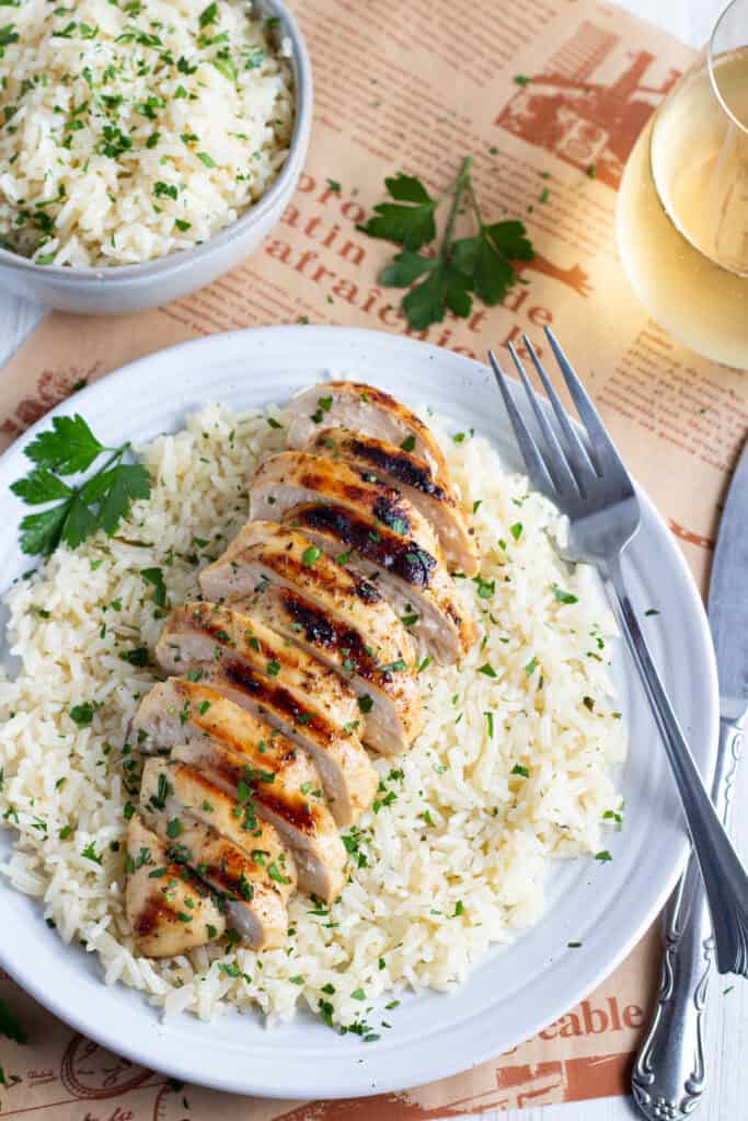 White plate of rice topped with a sliced grilled chicken breast.