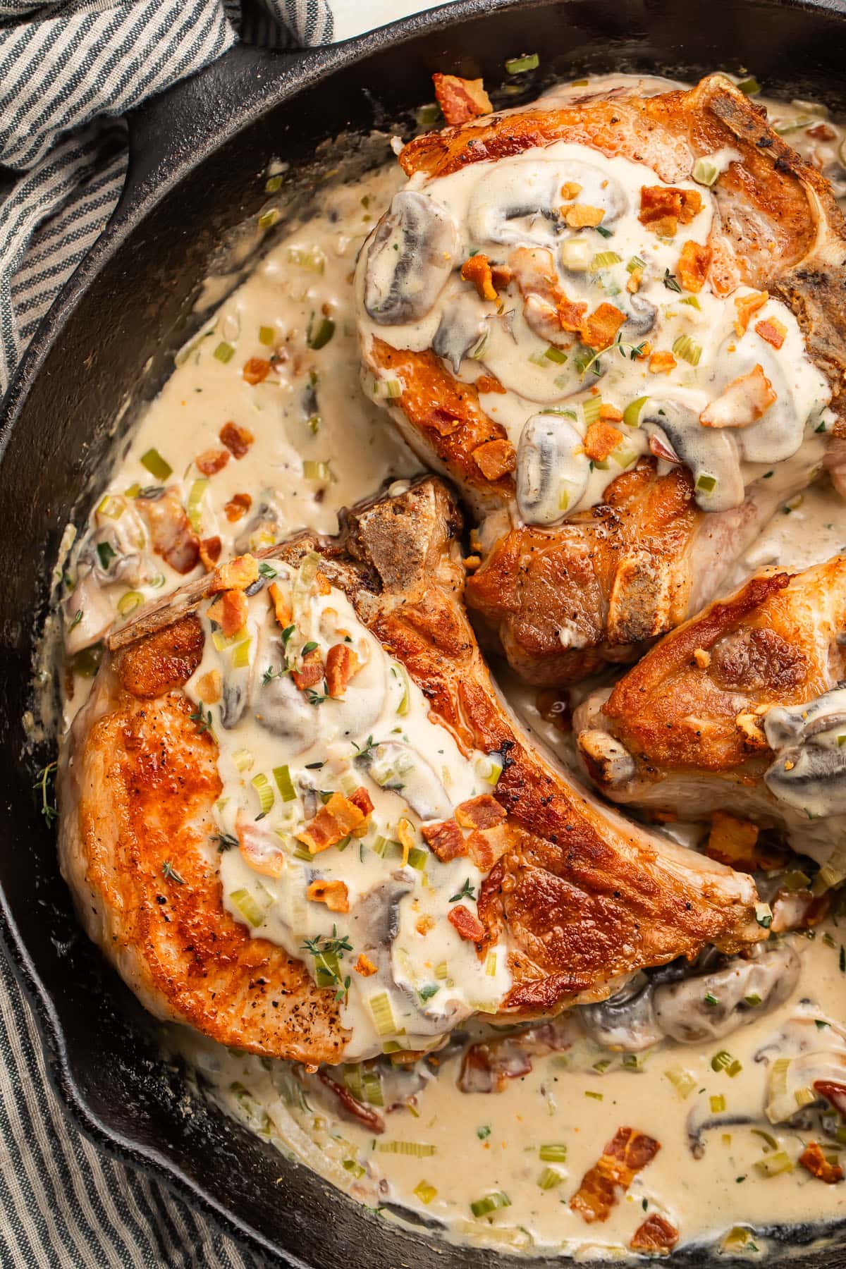 Keto smothered pork chops in a cast iron skillet with a creamy sauce.