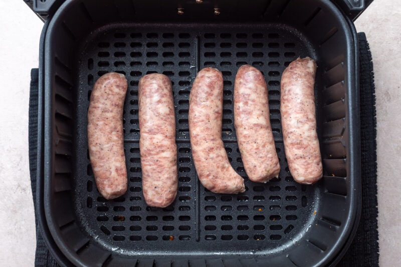 5 uncooked Italian sausage links in an air fryer basket.
