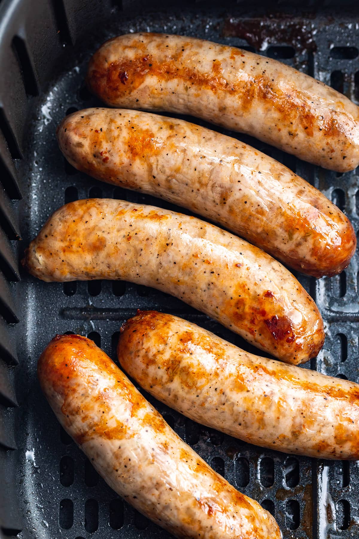 Close up of Italian sausages cooked in an air fryer basket.