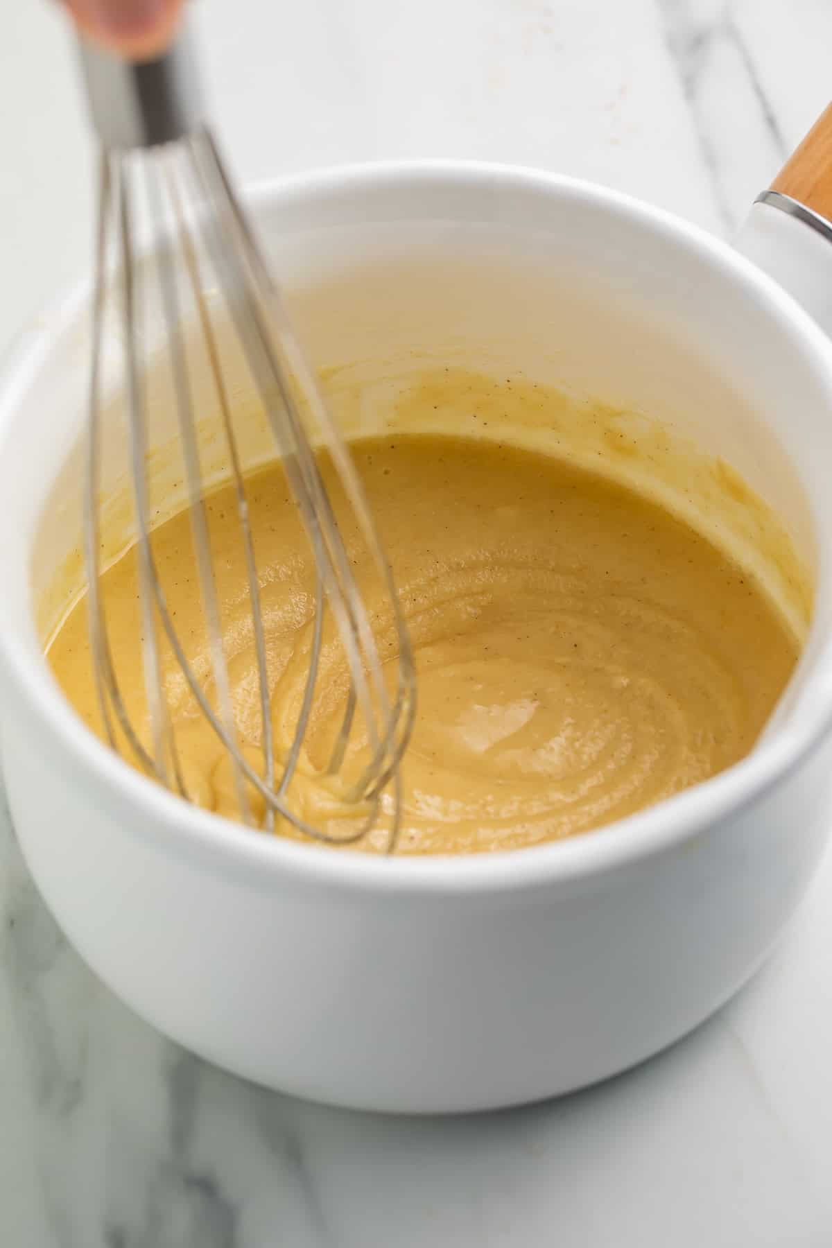 Whisk suspended against a finished white saucepan of gluten free roux.