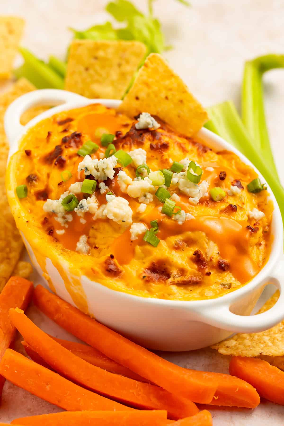 Buffalo chicken dip in an oval baking dish garnished with crumbled cheese and sliced salad onions. 