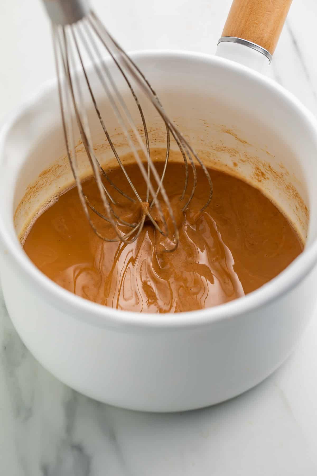 In progress gluten free roux being whisked in a white saucepan with a wooden handle. 