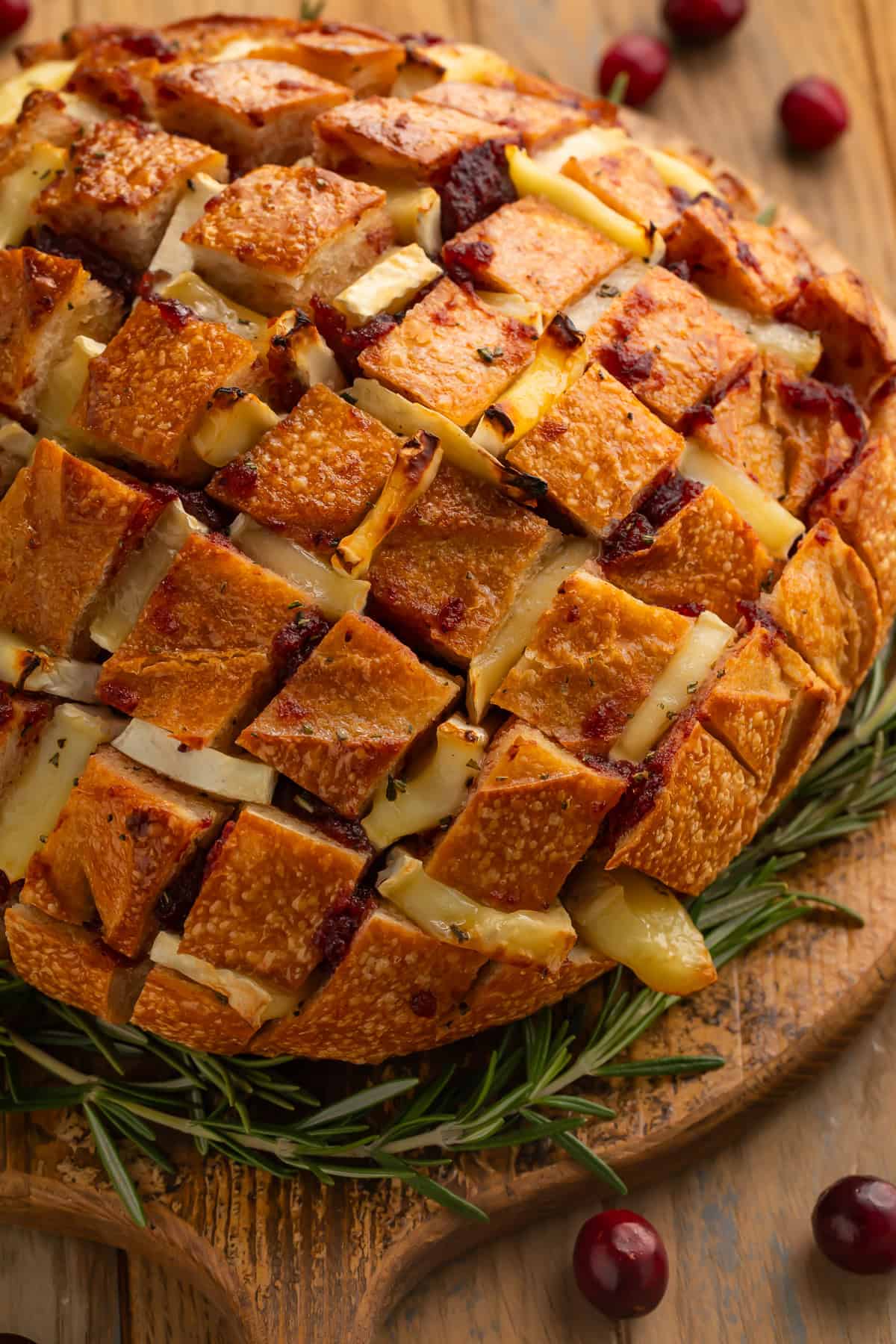 A side-on view of a baked brie pull apart bread with cranberries and rosemary.