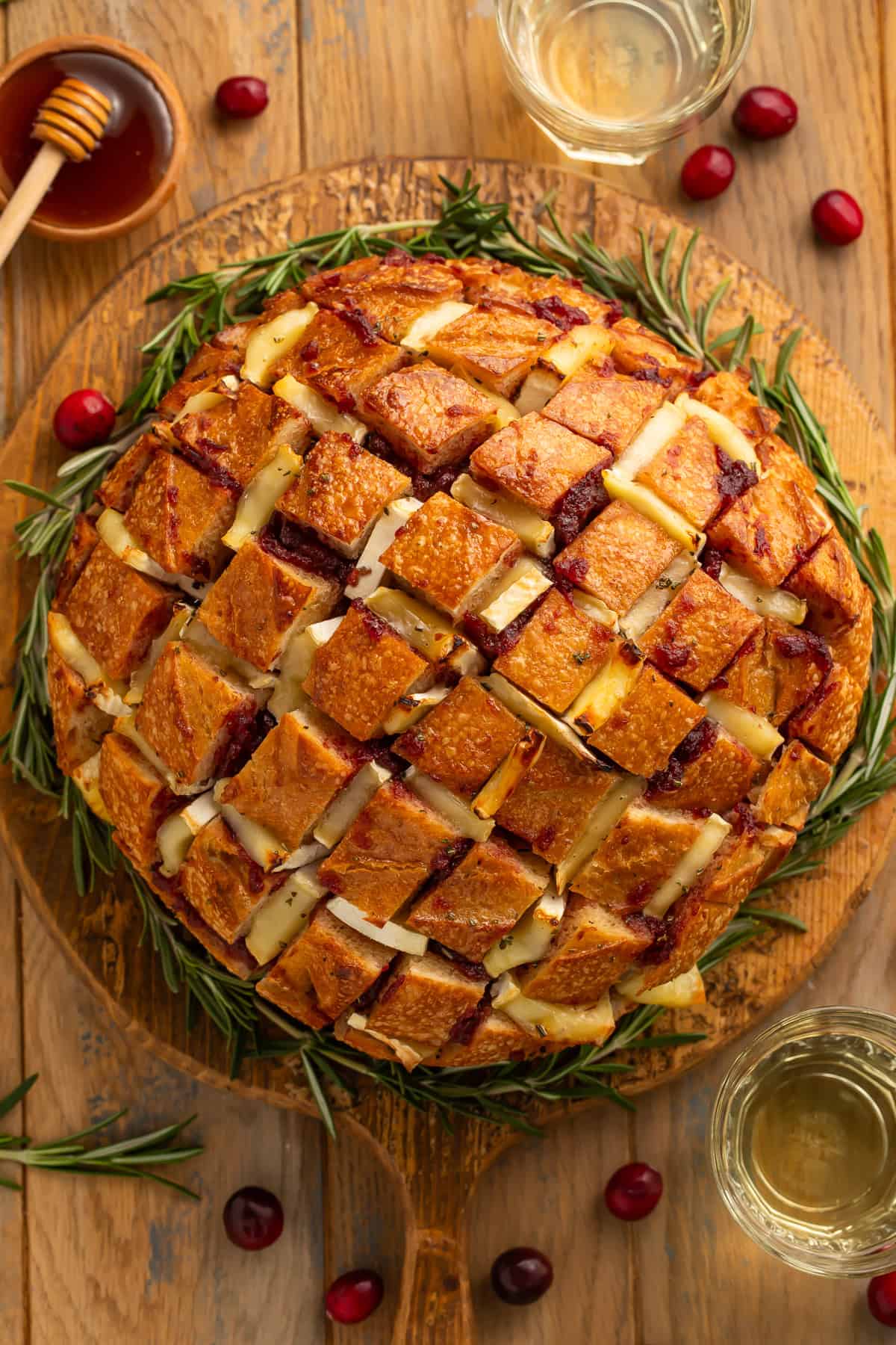 Top down view of a cranberry brie pull apart bread on a wooden board garnished with rosemary sprigs around it like a wreath.