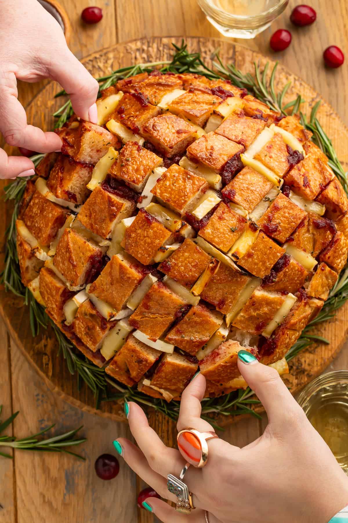 Two sets of hands reaching in to take pieces of cranberry pull apart bread.
