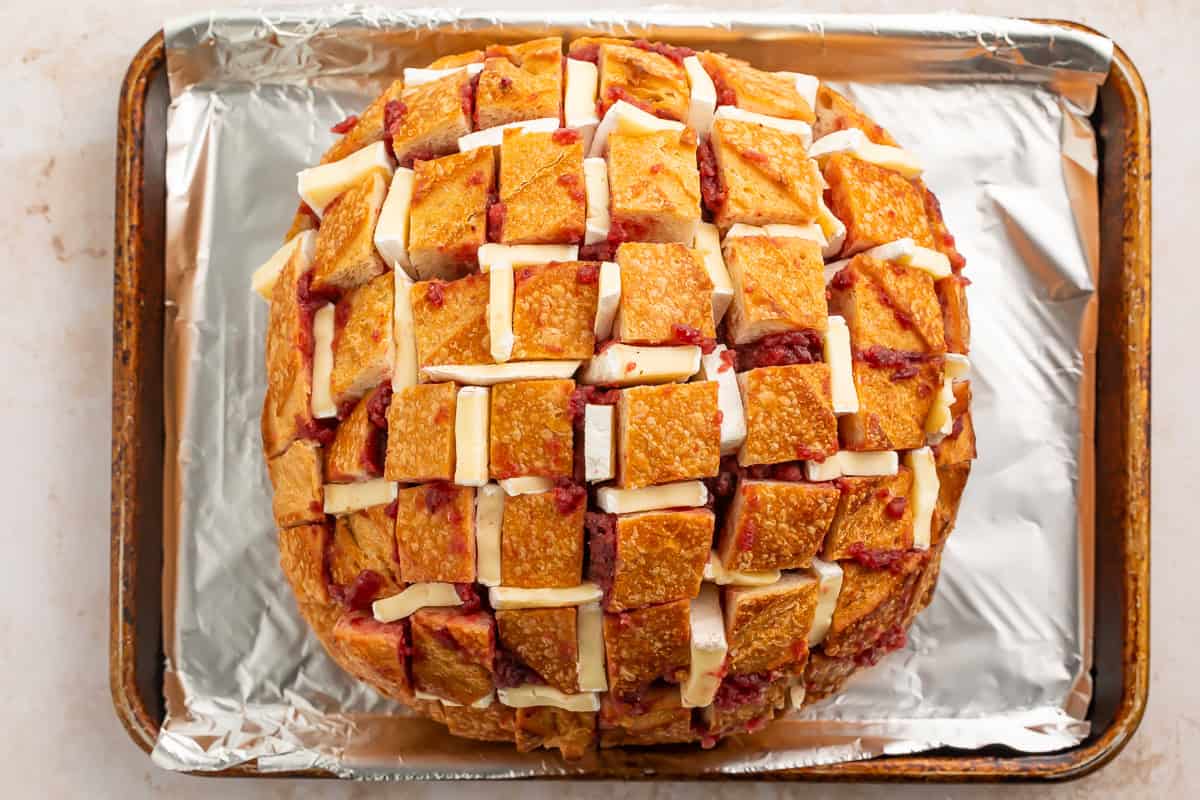 An uncooked cranberry brie pull apart sourdough on a foil-lined baking sheet.