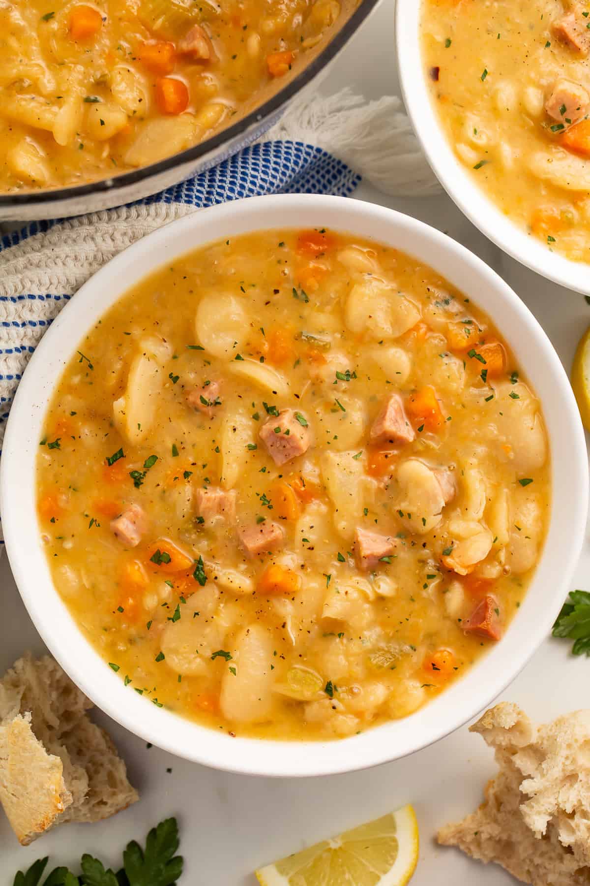 Close up of a white bowl of lima bean soup with another bowl and the casserole pot visible off to the side.