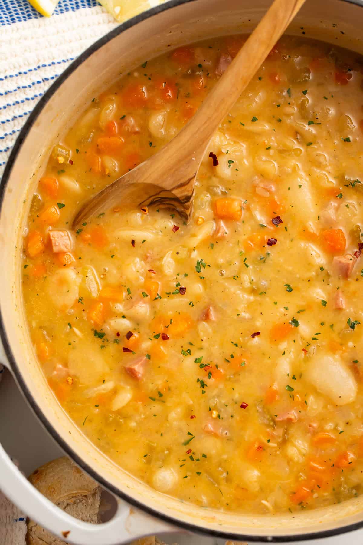 Wooden spoon being stirred in a white dutch oven of lima bean soup.