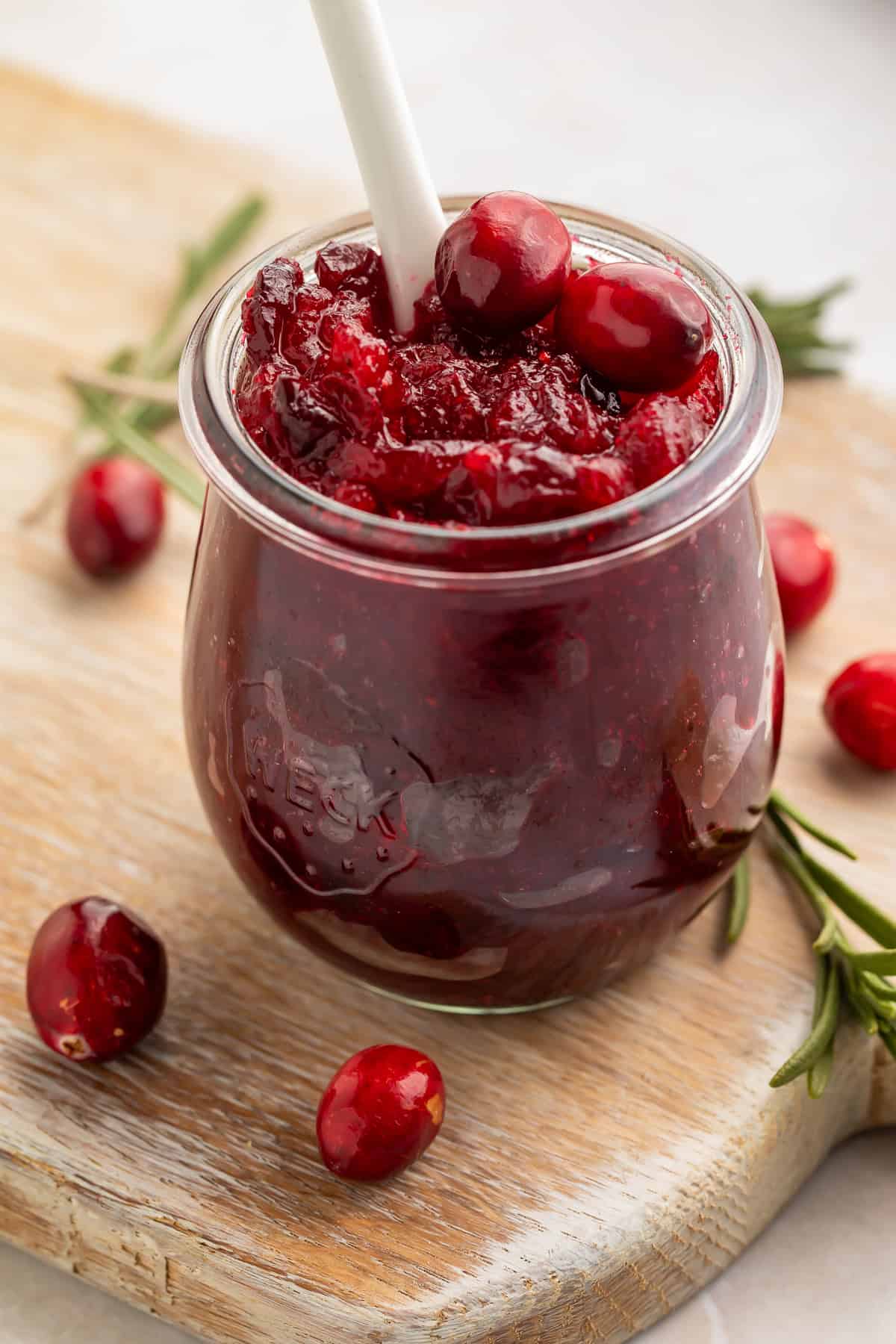 Close up of a jar of homemade cranberry jam garnished with fresh cranberries and rosemary sprigs.