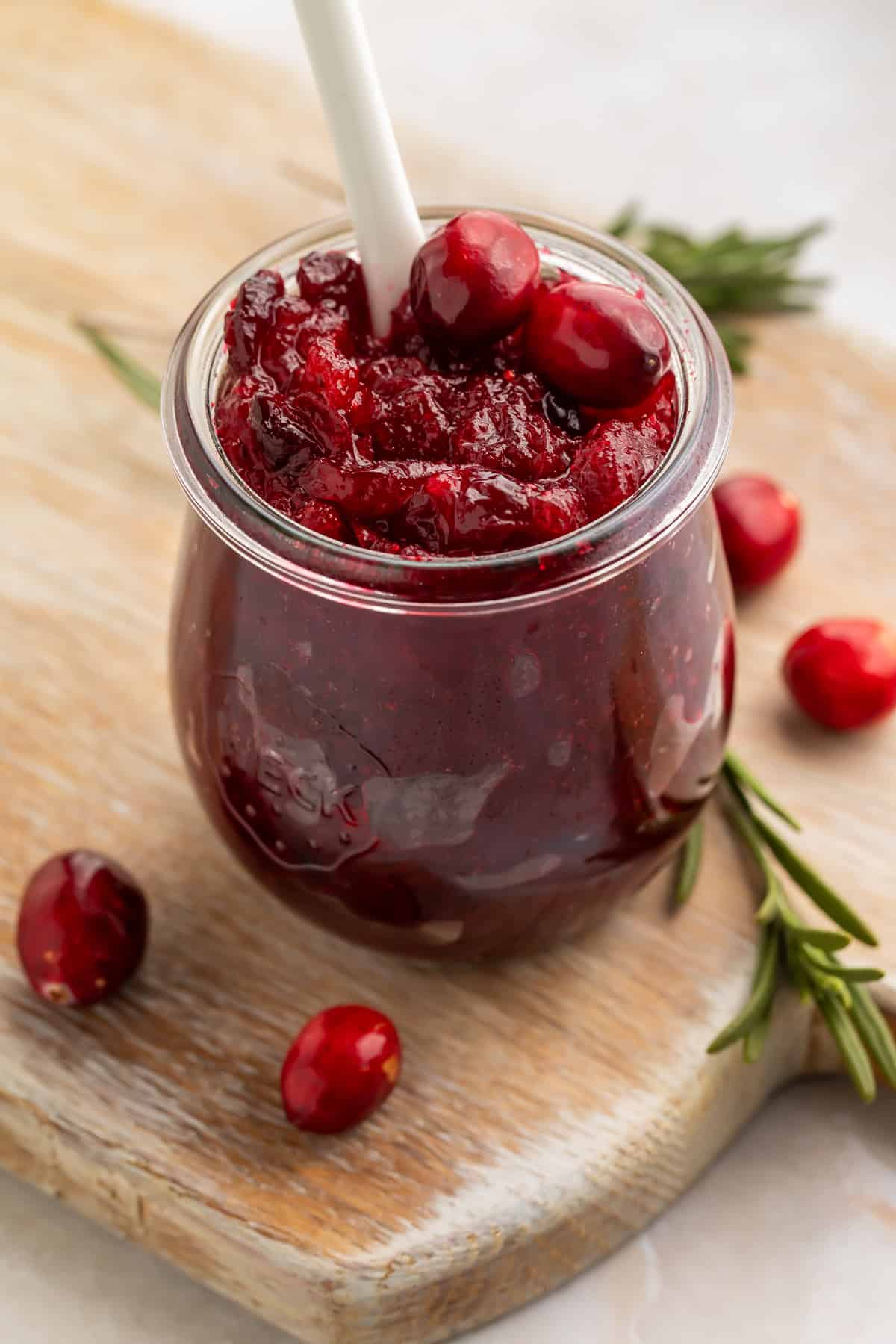 Jar of cranberry jam with a white spoon sticking out of the top.