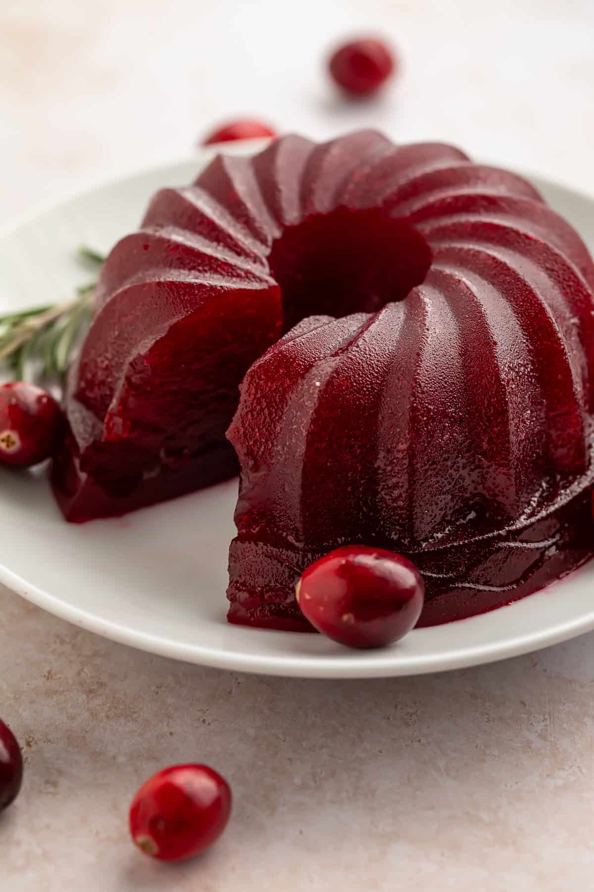 Jellied cranberry sauce made in a bundt pan on a white plate with a slice taken out of the side.
