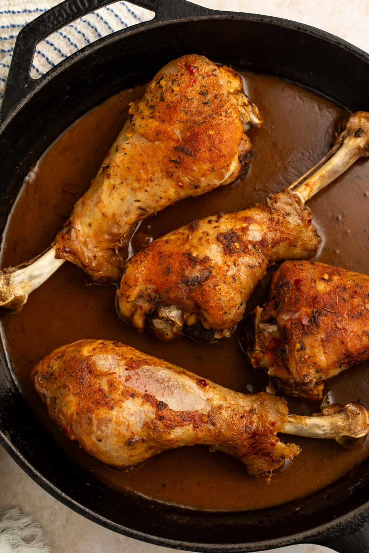 Close up of four roasted turkey legs in a cast iron skillet of dark brown gravy.