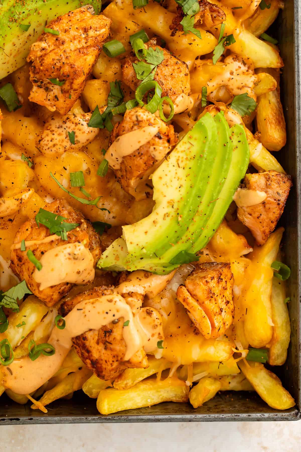 Close up of sliced avocado, Cajun salmon pieces and French fries in a metal tray.