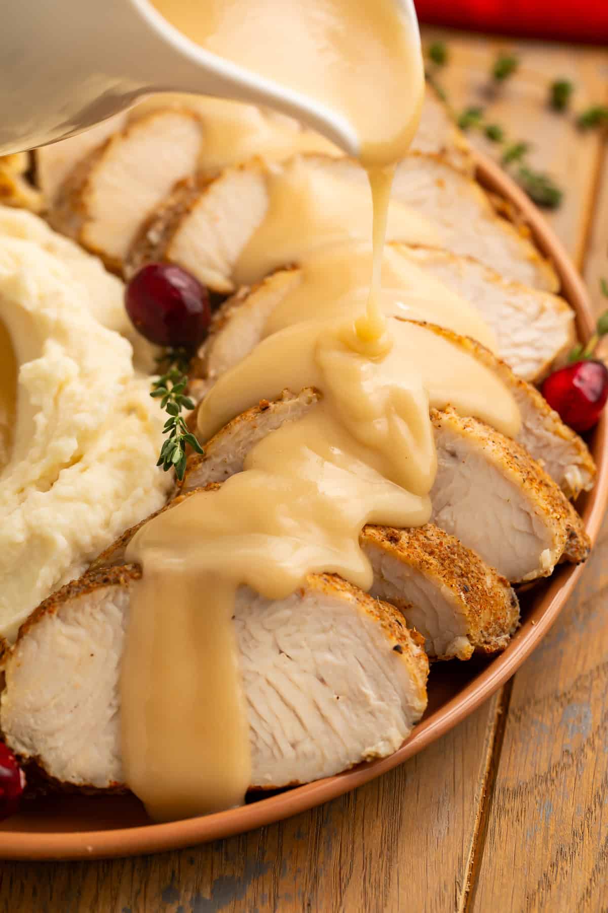 Gravy being poured over sliced turkey tenderloin on a plate with Thanksgiving sides.